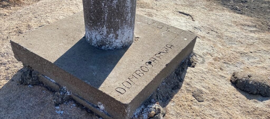 Concrete survey marker with 'DOMBOSHAVA' engraved on the base, set into the rocky surface of Domboshava Hill in Zimbabwe.